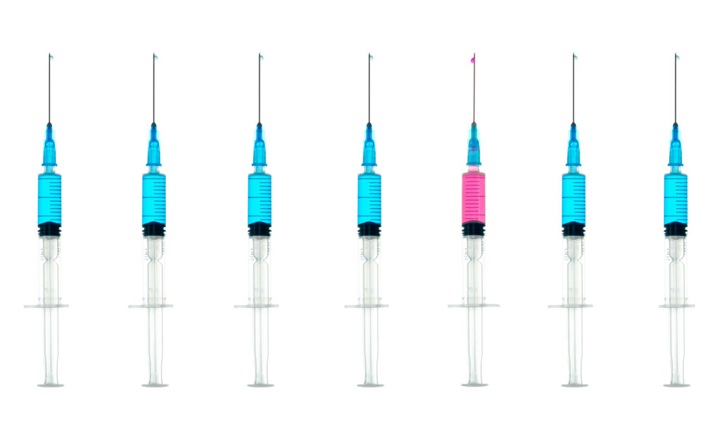 a row of syringes, all filled with blue liquid, other than a single pink one