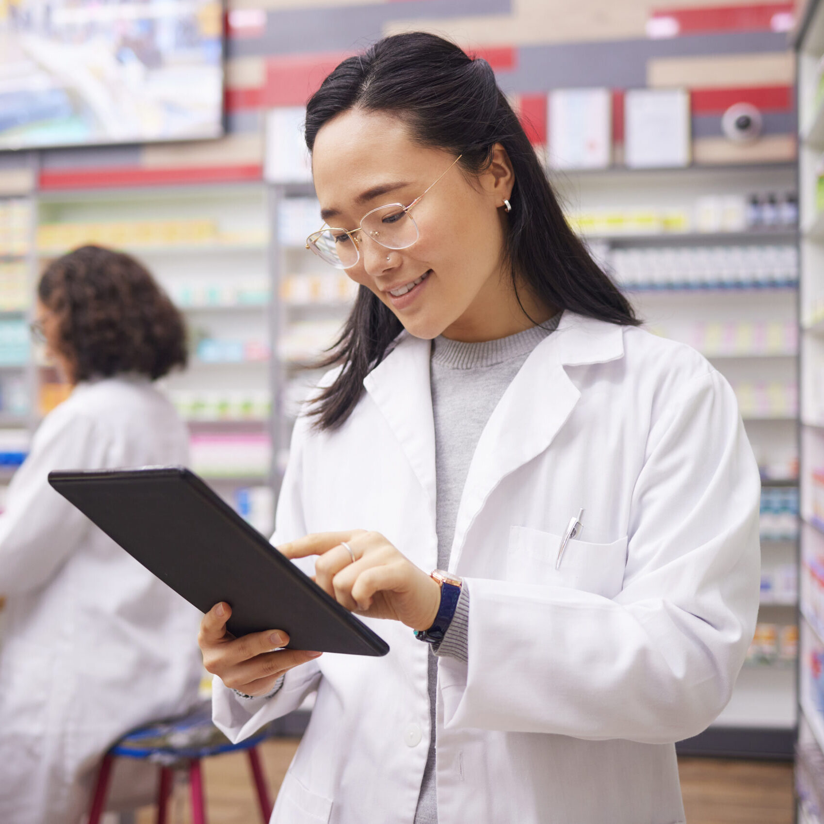 A pharmacist in a pharmacy checking prescriptions on a tablet
