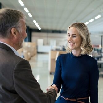 Happy,Blond,Businesswoman,Handshaking,With,Colleague,At,Warehouse